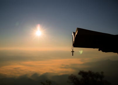 Silhouette of human hand holding bible and cross, the background