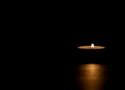 Lit tin candle in the dark conveying memorial, death, hope or darkness