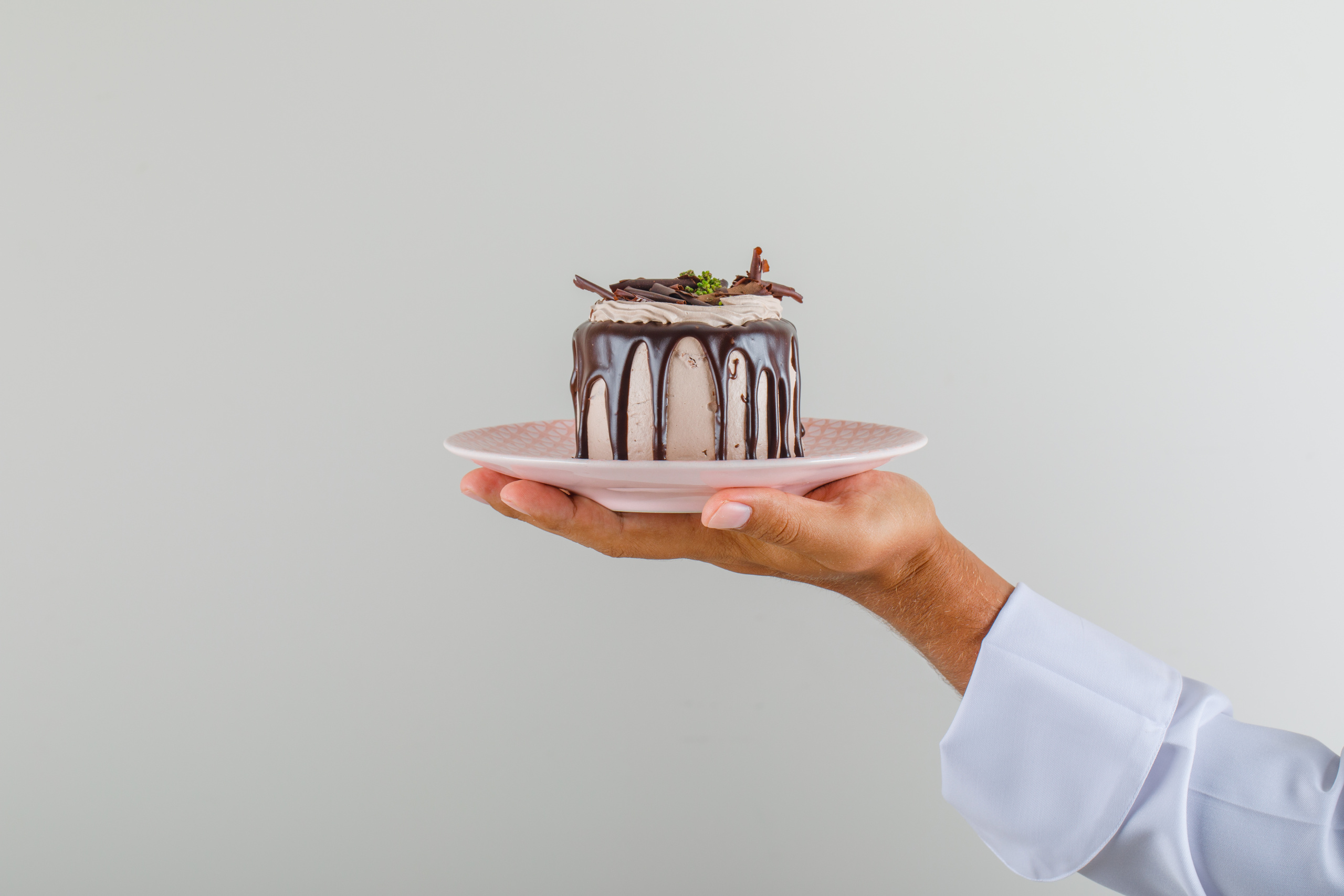 Male chef cook in uniform holding dessert cake in plate , front view.